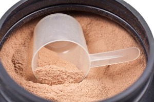 Scoop of chocolate whey isolate protein in black plastic contain